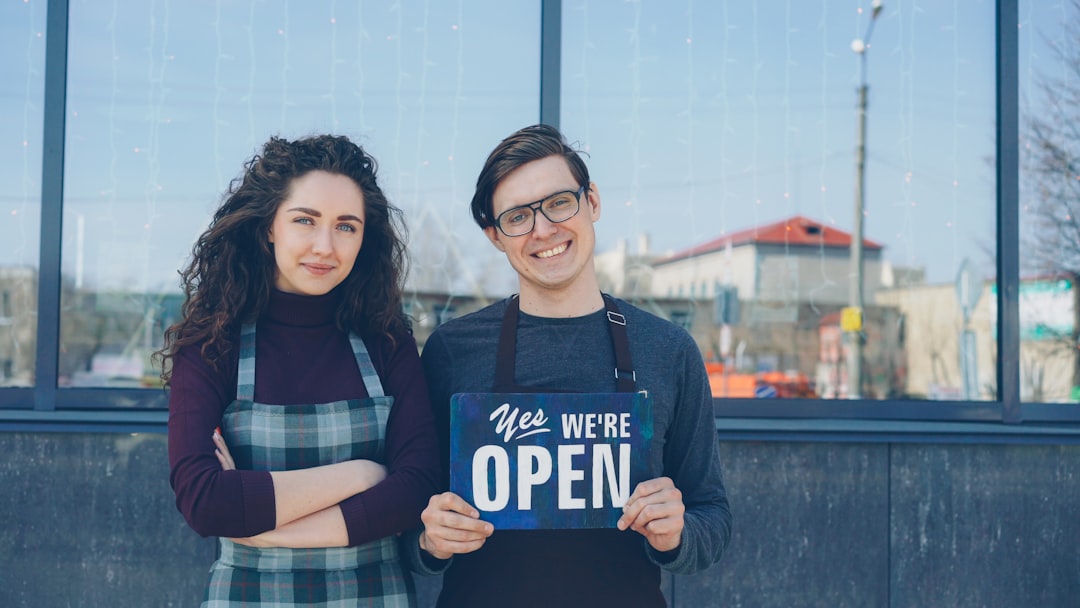 Two business owners holding a We Are Open sign in front of their storefront